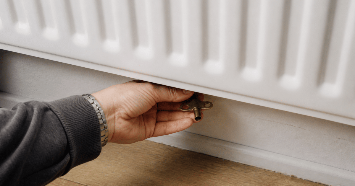 Main tenant une cle sous un radiateur blanc