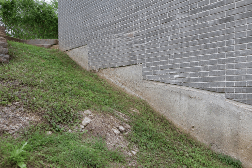 Mur de brique gris sur terrain en pente avec fondations visibles